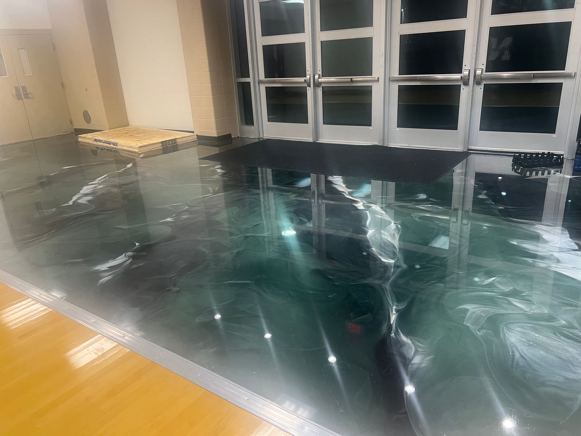 Dark, shiny floor with light streaks near glass doors. Wooden pallet near door.
