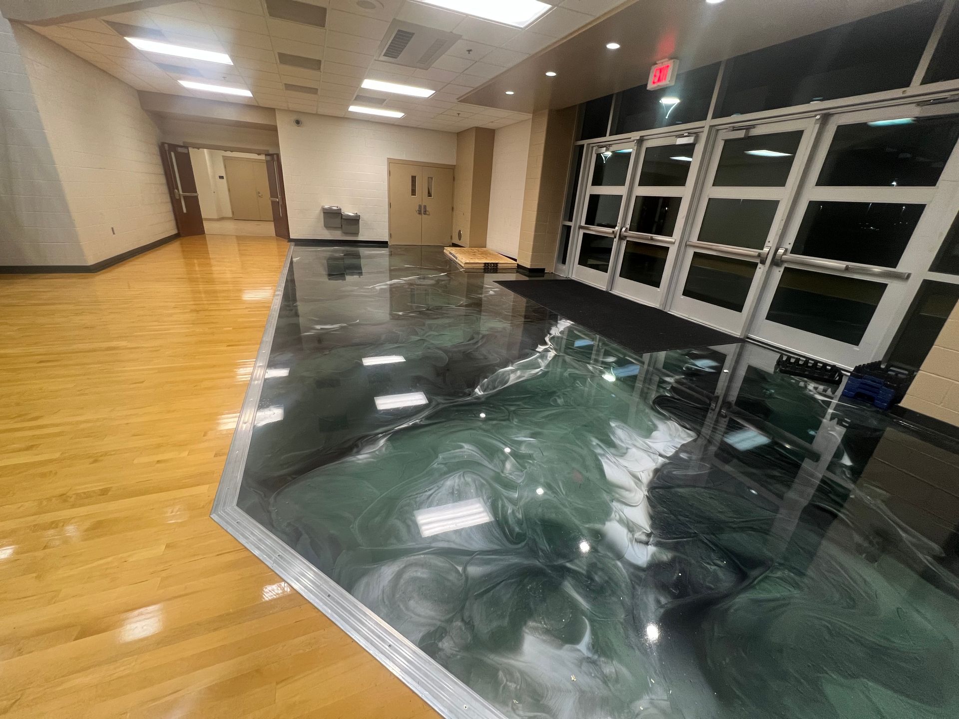 Hallway with a green epoxy floor and wooden floor, near glass doors.