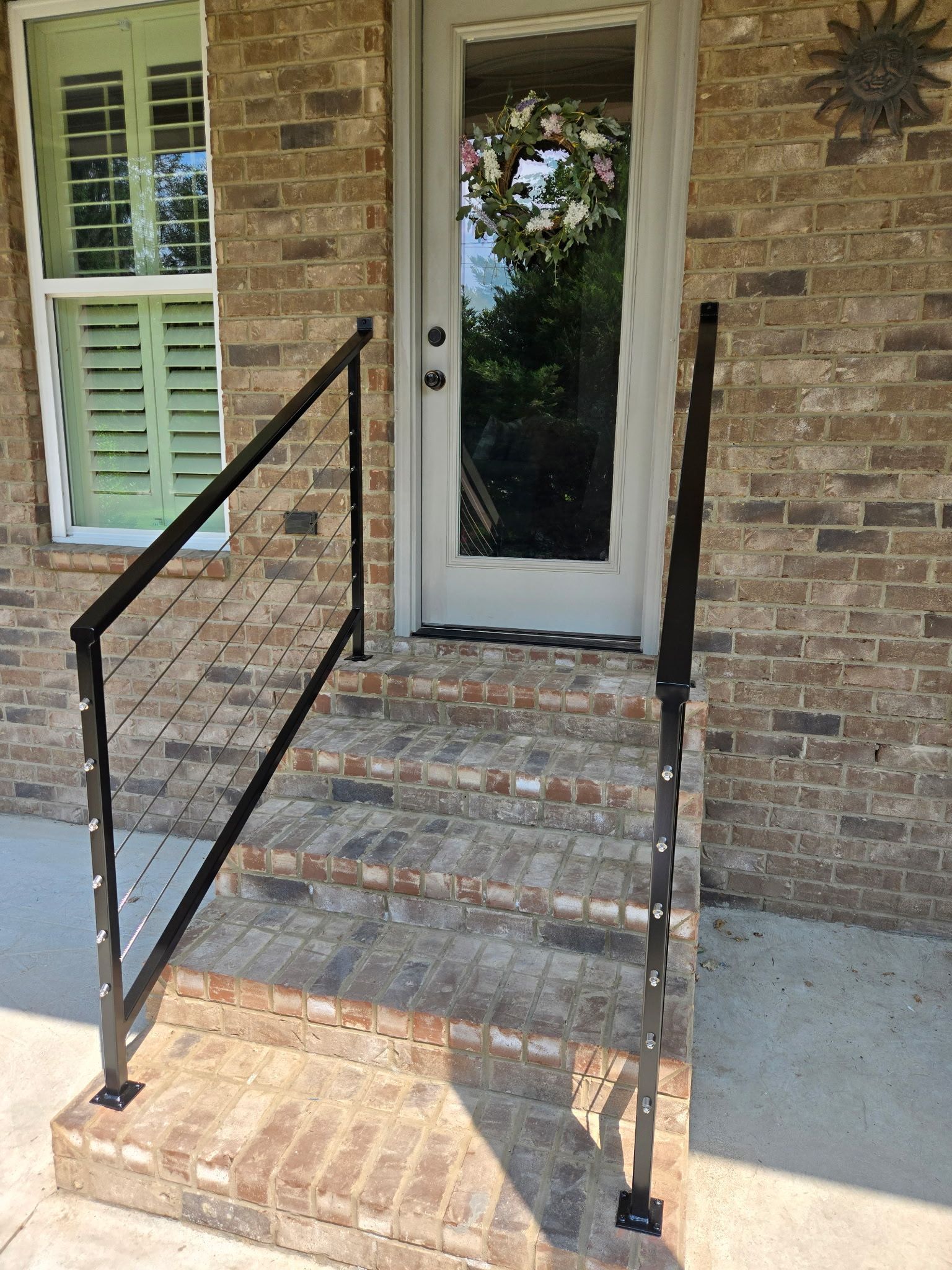 A brick house with a black railing and stairs leading to the front door.