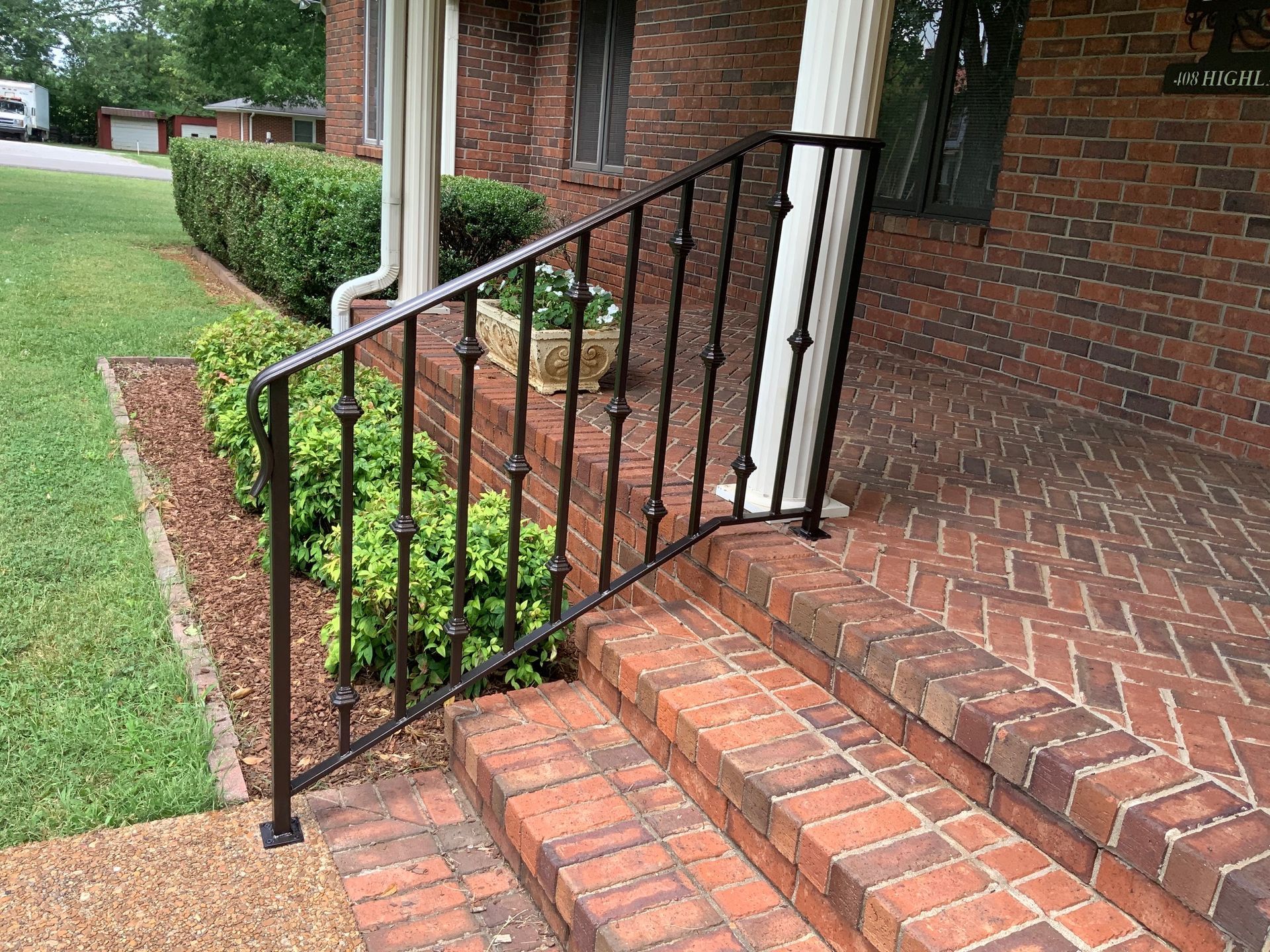 There is a wrought iron railing on the steps of a brick house.