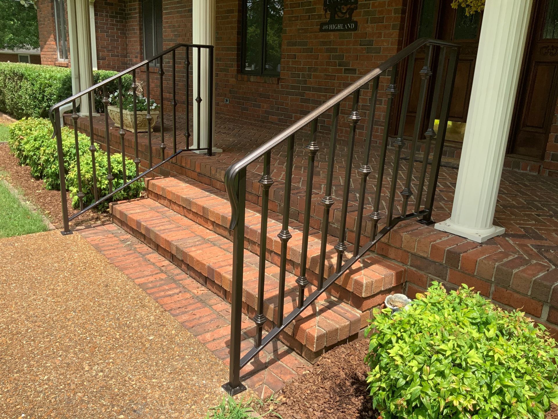 There is a wrought iron railing on the porch of a brick house.