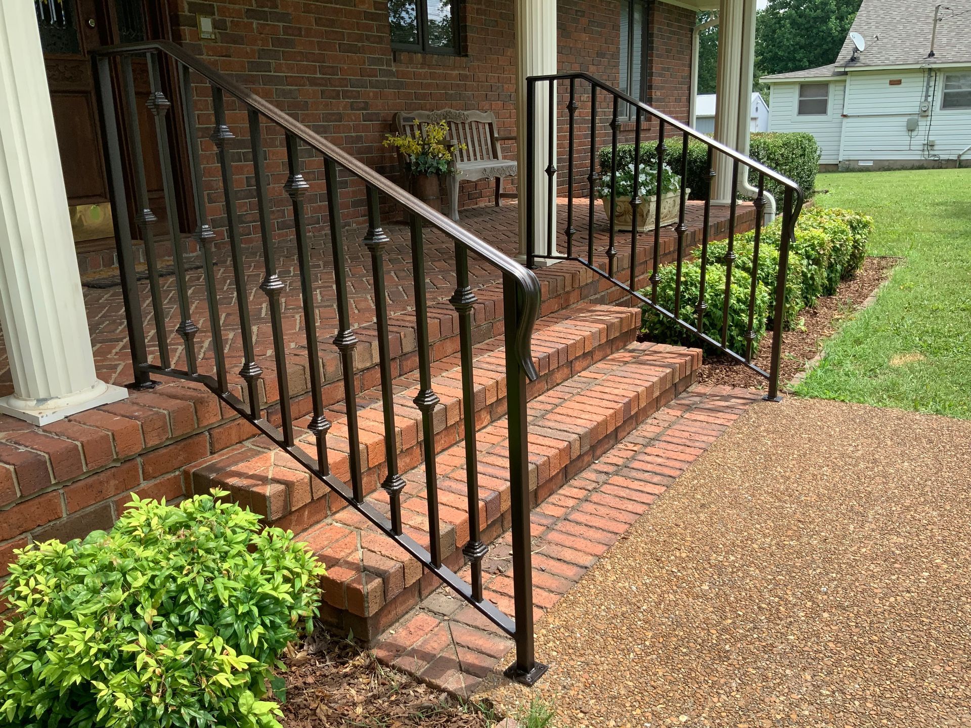 There is a wrought iron railing on the porch of a brick house.