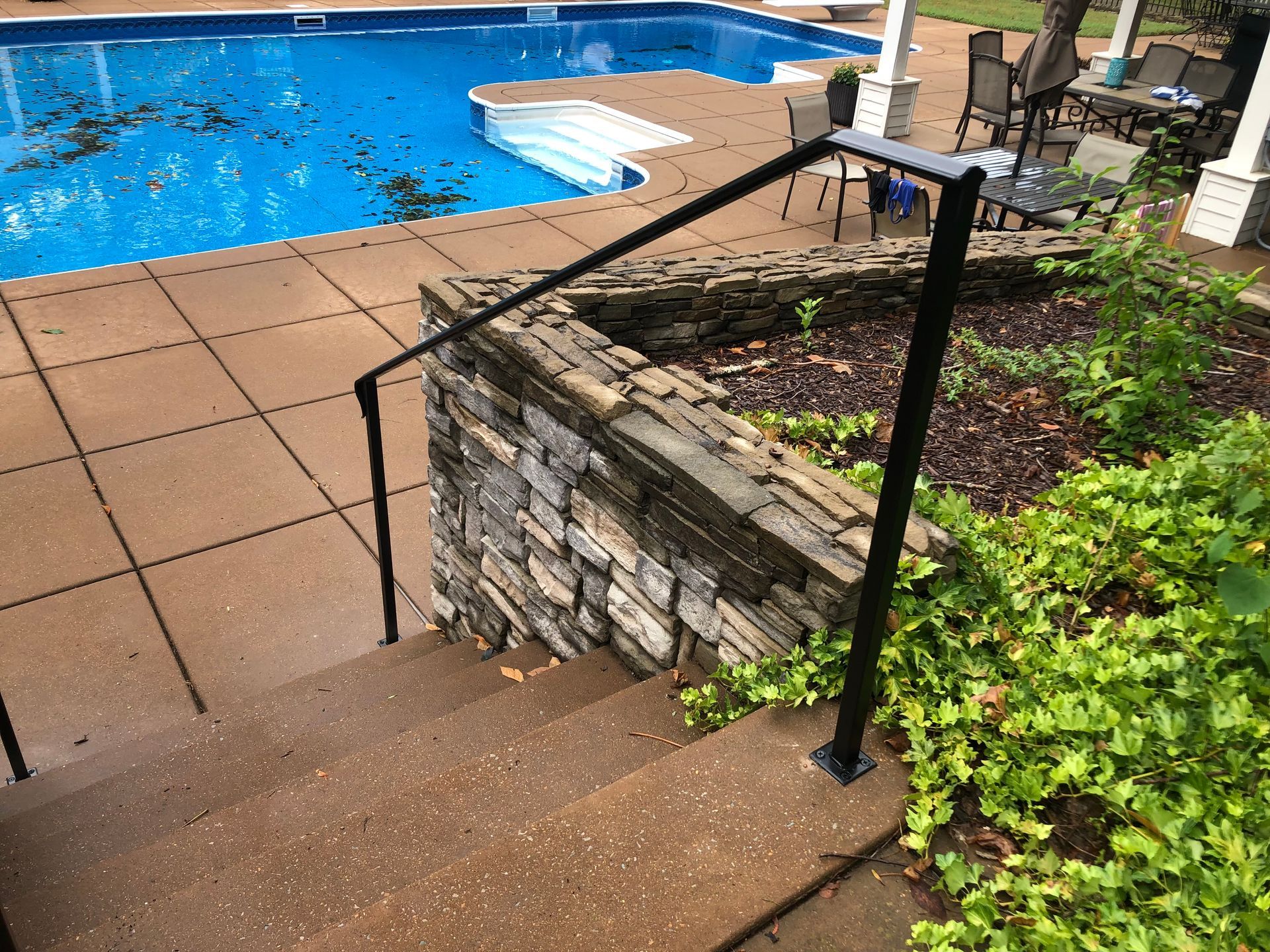 A staircase leading to a swimming pool with a black railing.