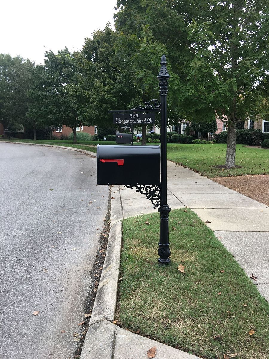 A black mailbox is sitting on the side of the road next to a sidewalk.