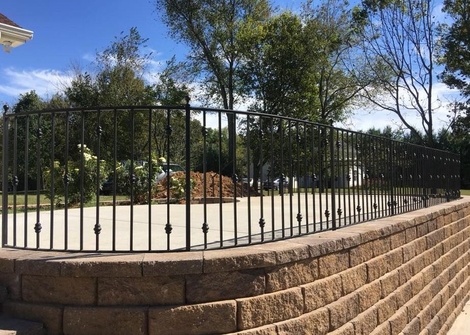A wrought iron fence is surrounding a brick wall.