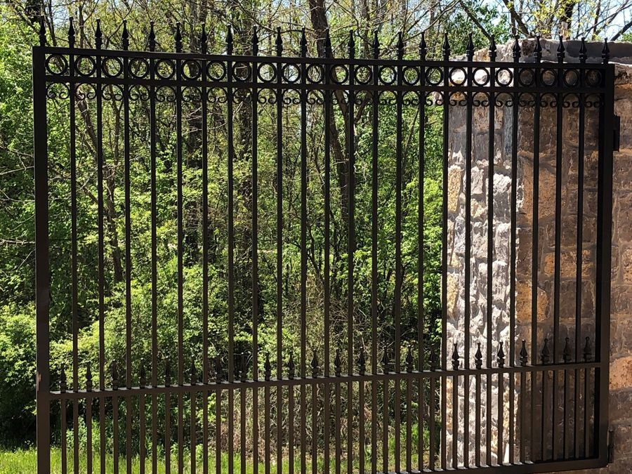A wrought iron gate is surrounded by trees and a stone wall.