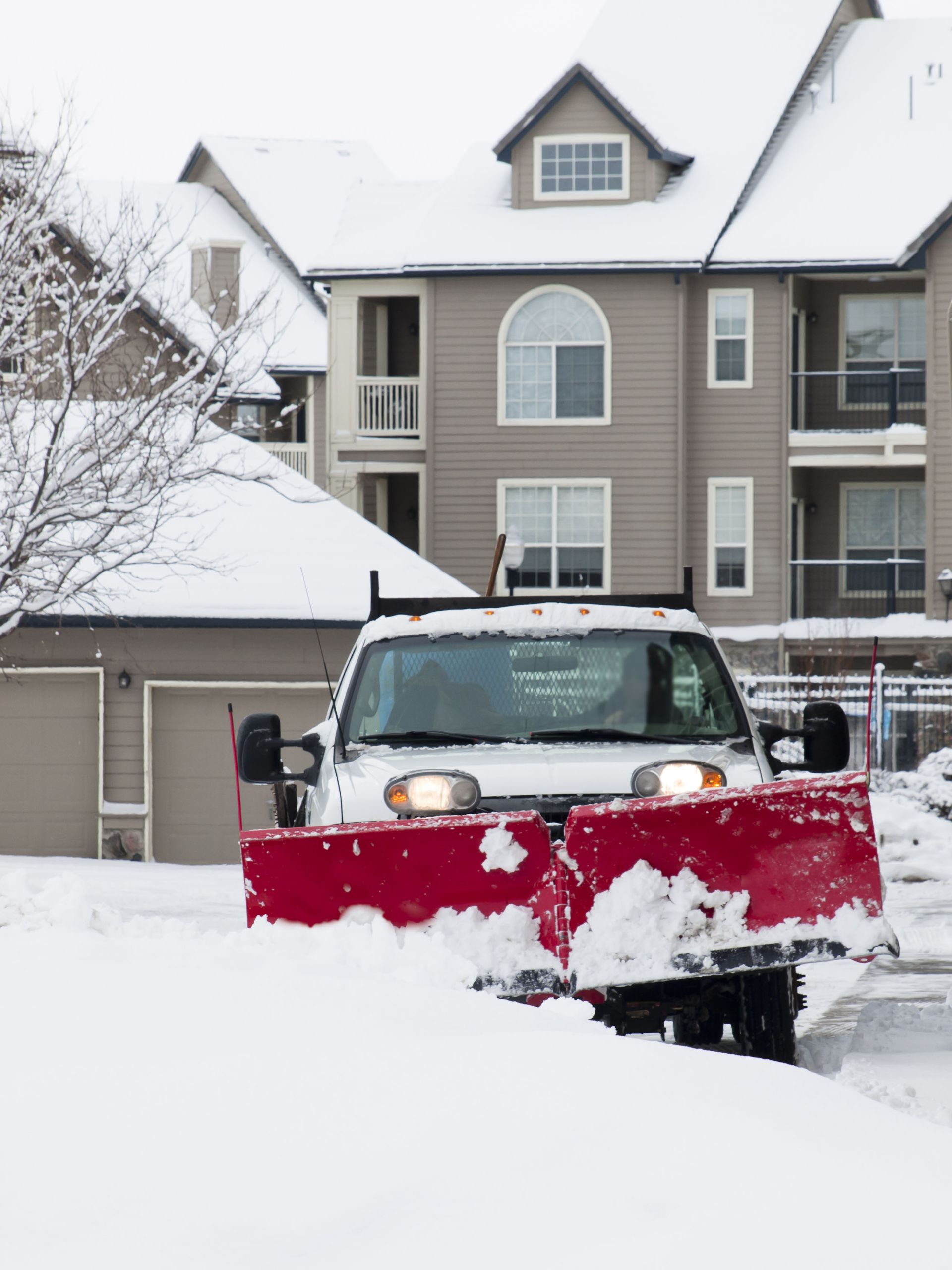 A red snow plow is clearing snow in front of a condo complex