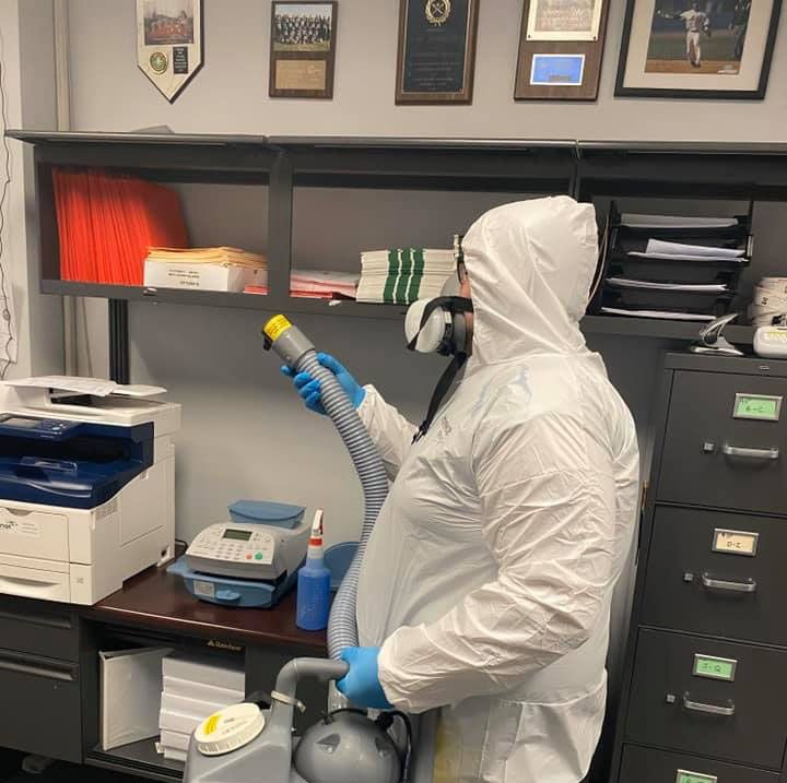Person in hazmat suit sanitizing an office with a sprayer.