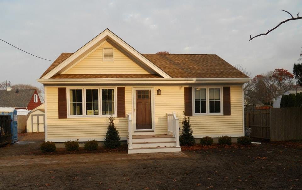 Yellow house with brown roof and trim; front steps, brown shutters, and small bushes.