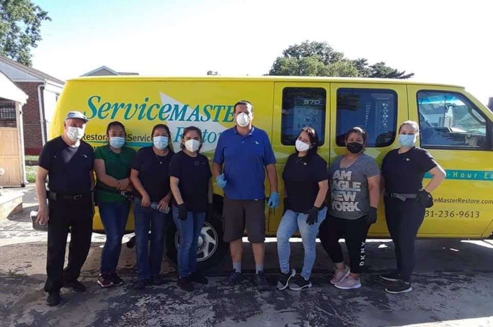 Group of ServiceMaster employees stand by a yellow van. They are wearing masks and gloves.