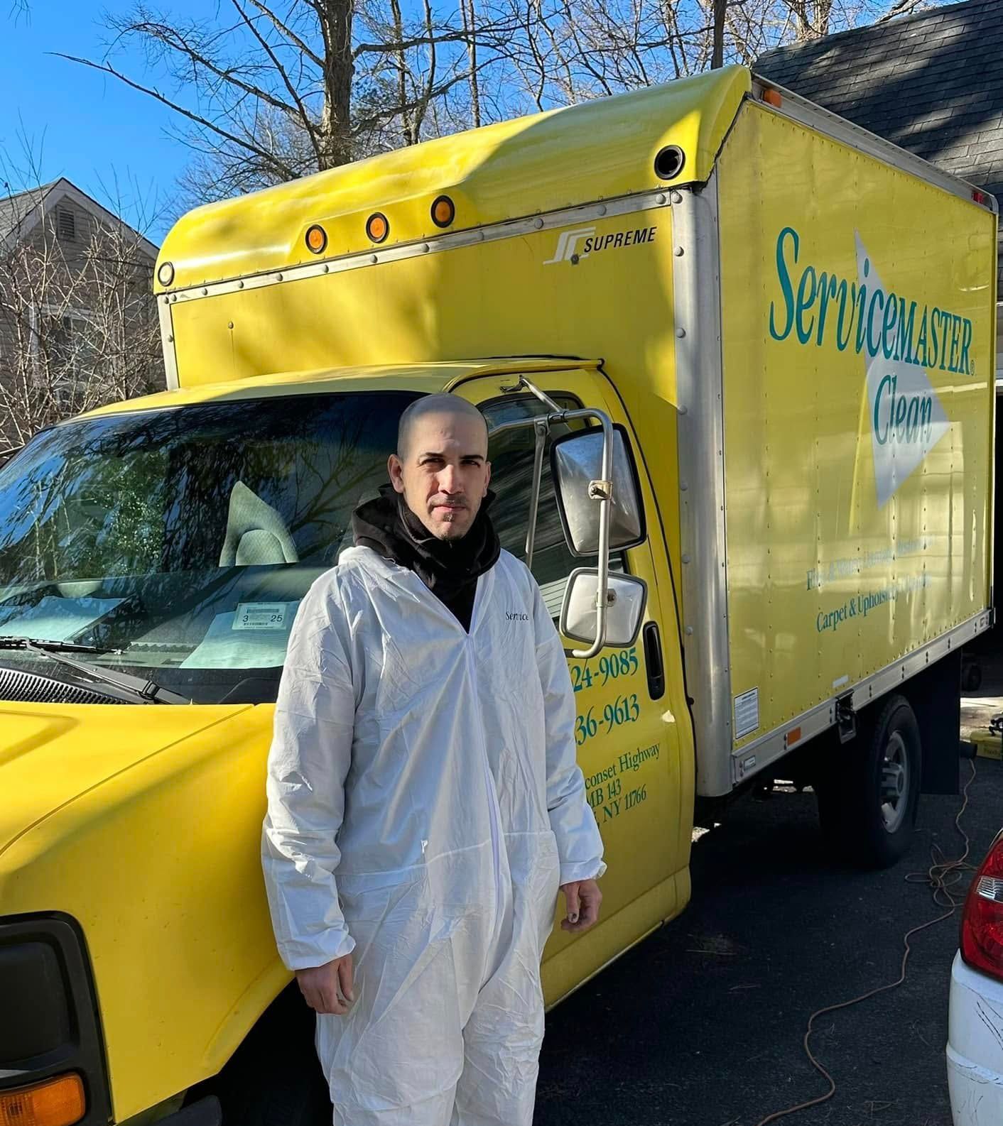 Man in white protective suit stands next to a yellow ServiceMaster truck.