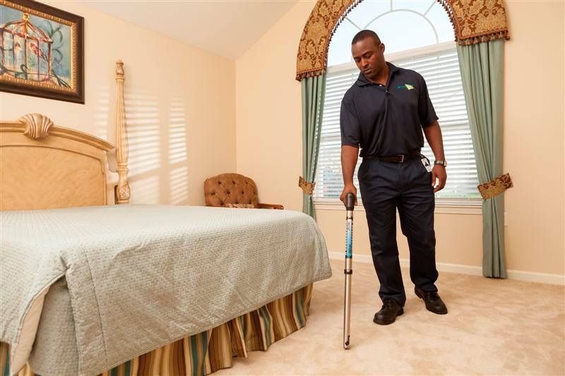 Man in uniform using cane in a bedroom with a bed, window, and chair.