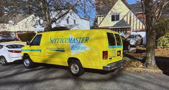 Yellow ServiceMaster Restore van parked on a street in front of houses.
