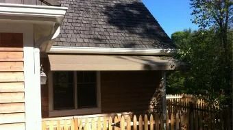 House exterior with tan siding, dark shingled roof, and a small fenced patio under a blue sky