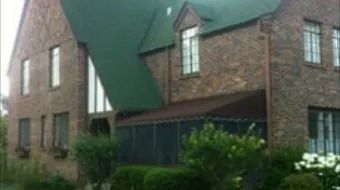 Brick house with a green roof and screened porch, viewed from the front yard.