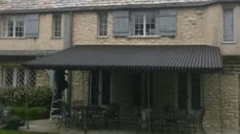 Stone townhouse with a dark awning over a covered front porch and patio seating