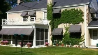 Two-story house with beige siding, white trim, awnings, balcony, and flower boxes beside a green lawn