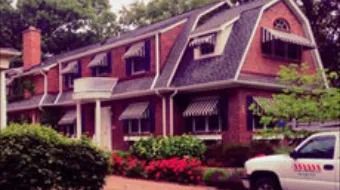 Red brick house with steep roofs and dormers, surrounded by bushes and pink flowers, with a white truck parked outside.
