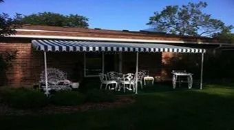 Brick house patio with striped awning, white chairs, and a green lawn at dusk
