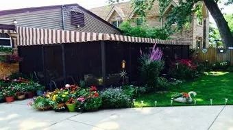 Backyard patio with striped awning, flower beds, and green lawn beside a driveway