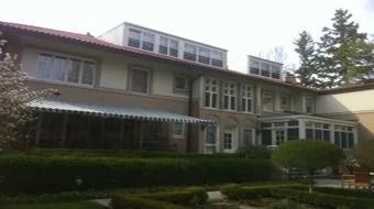 Large white two-story building with many windows, a hedge-lined garden, and trees in front.