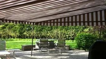 Patio with striped awning, tables, chairs, and lush green garden beyond