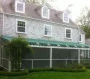 Two-story gray house with green awning and screened porch under leafy trees