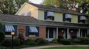Two-story house with striped awnings and a brick porch, lit warmly at dusk