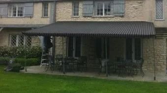 Stone house patio with a dark awning, outdoor seating, and green lawn.