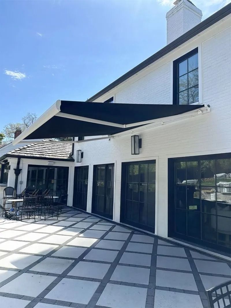 White patio with black awning, glass doors, and patterned stone flooring beside a building