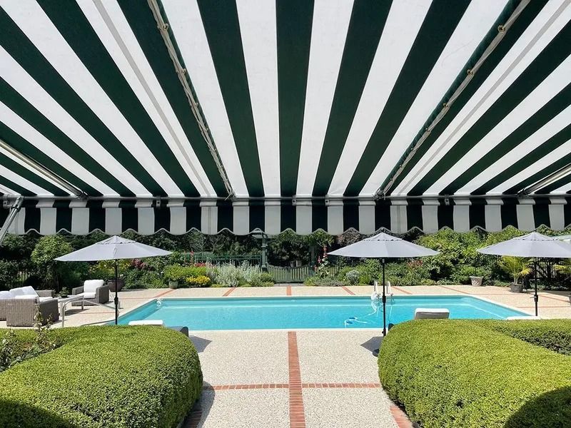 Poolside patio with striped canopy, turquoise pool, white umbrellas, and trimmed hedges