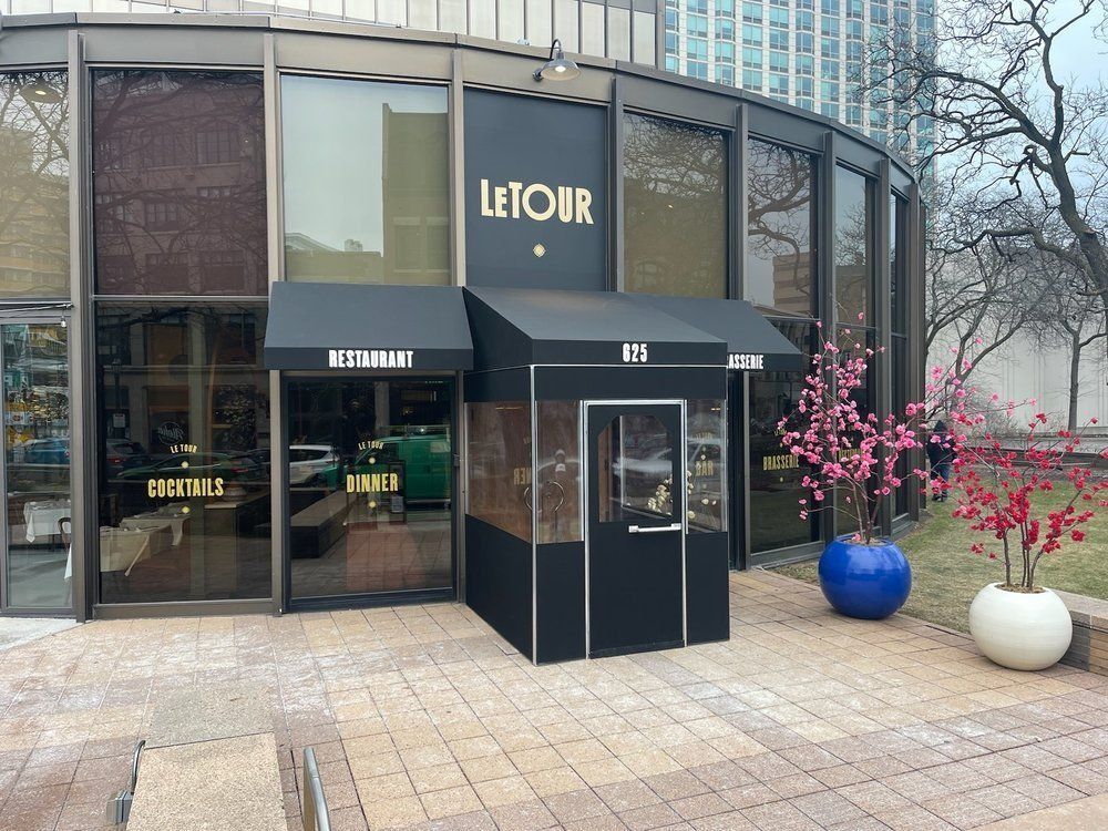 LeTOUR storefront with black awnings, glass facade, and potted flowers on a city sidewalk