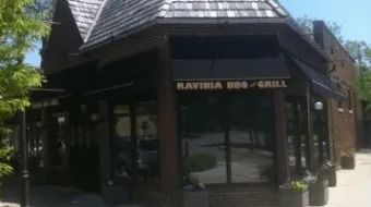 Small storefront with a dark roof and glass entrance, labeled “RAVINIA BBQ & GRILL.”