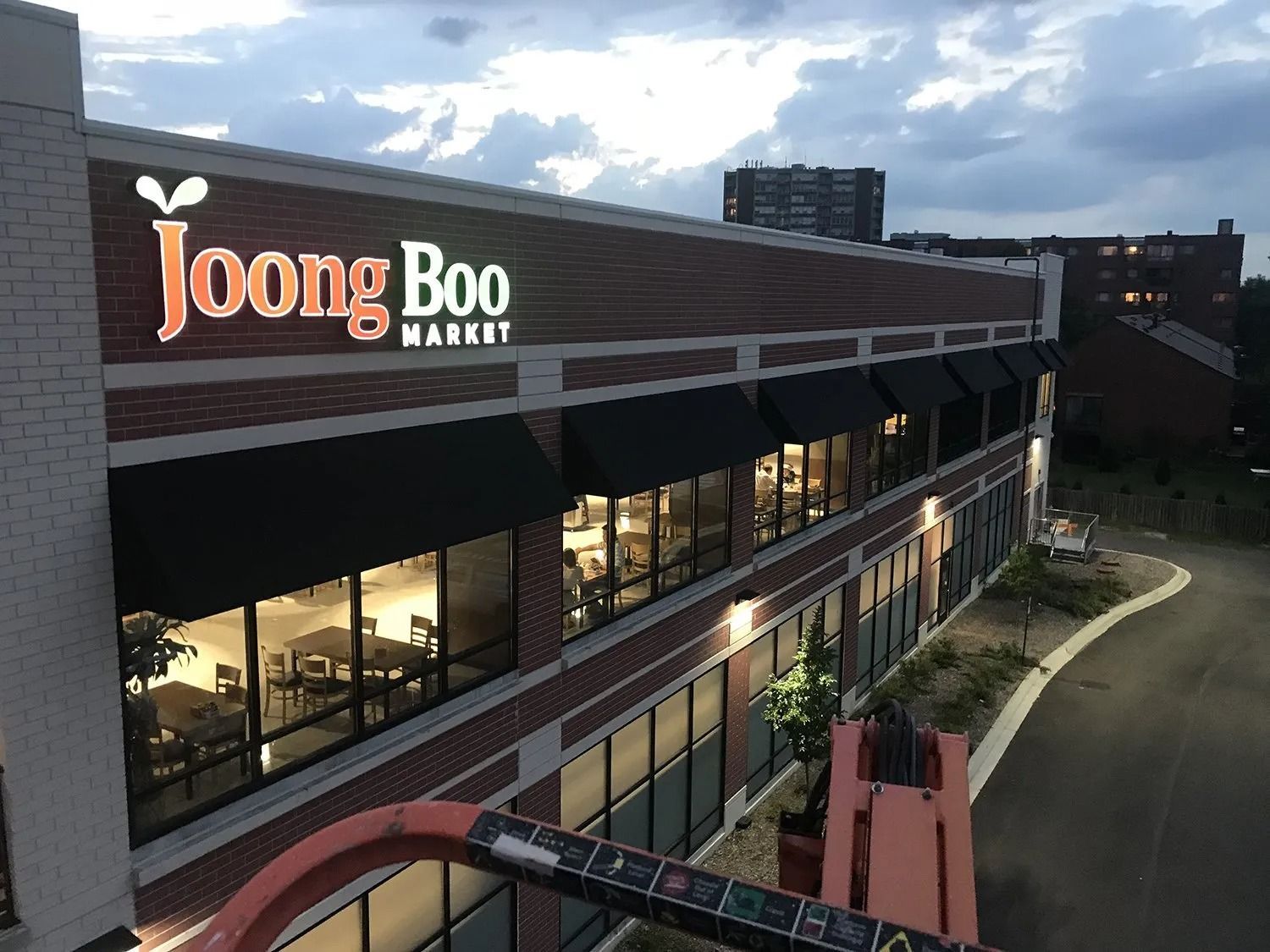 Joong Boo Market storefront at dusk, with lit windows and a curved walkway beside the building
