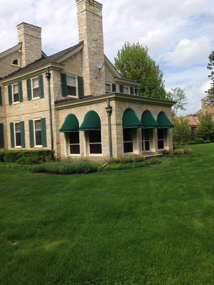 Stone house with green awnings and shutters, set on a grassy lawn under a cloudy sky