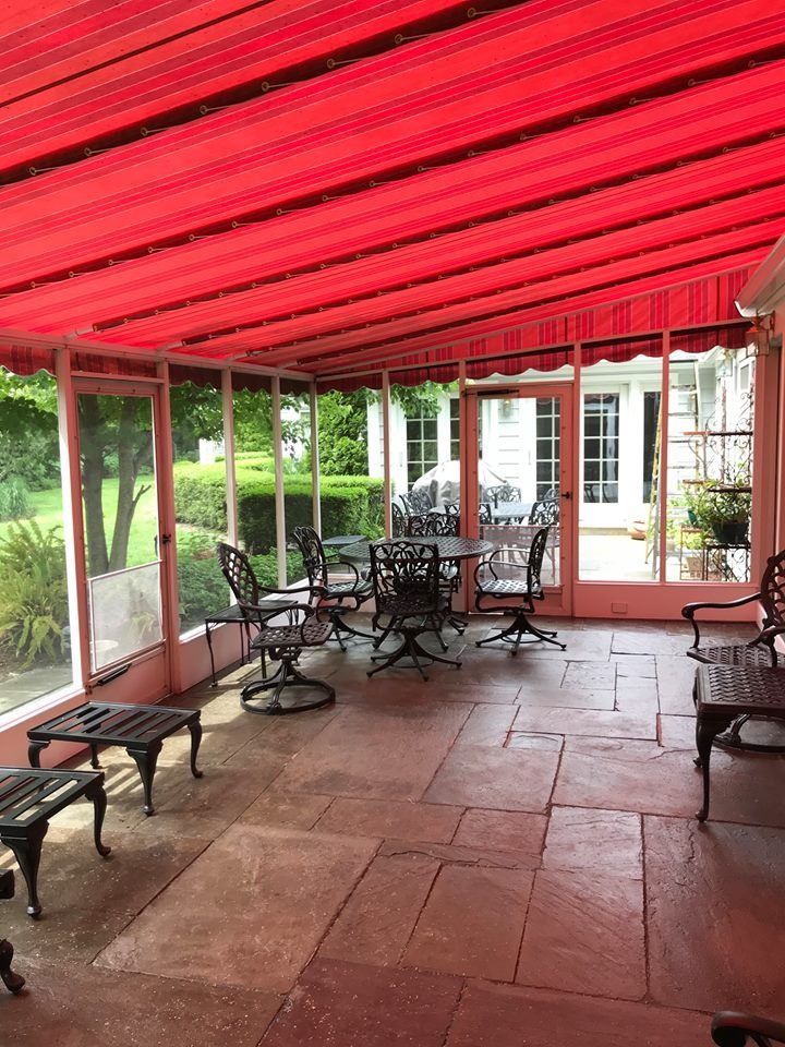 Covered patio with red striped awning, stone floor, and outdoor tables and benches overlooking a garden