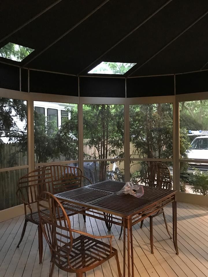 Screened porch with a wooden table, chairs, and views of trees outside.