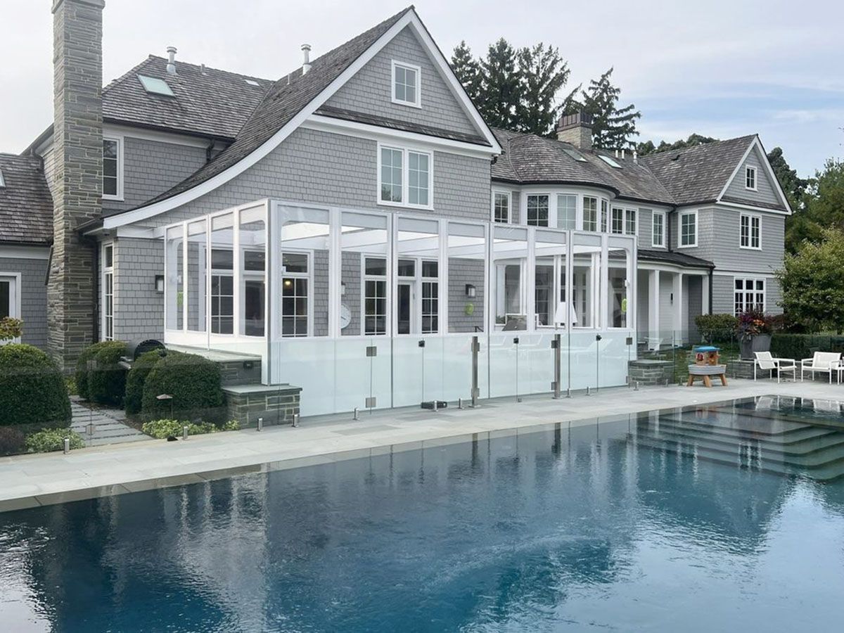 Gray house with white sunroom beside a backyard swimming pool