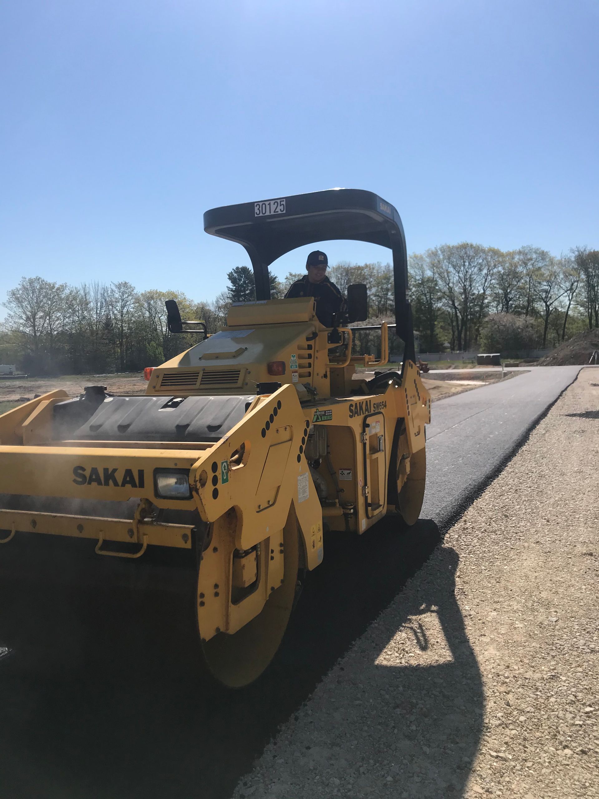 a man is driving a yellow Sakai roller on a road