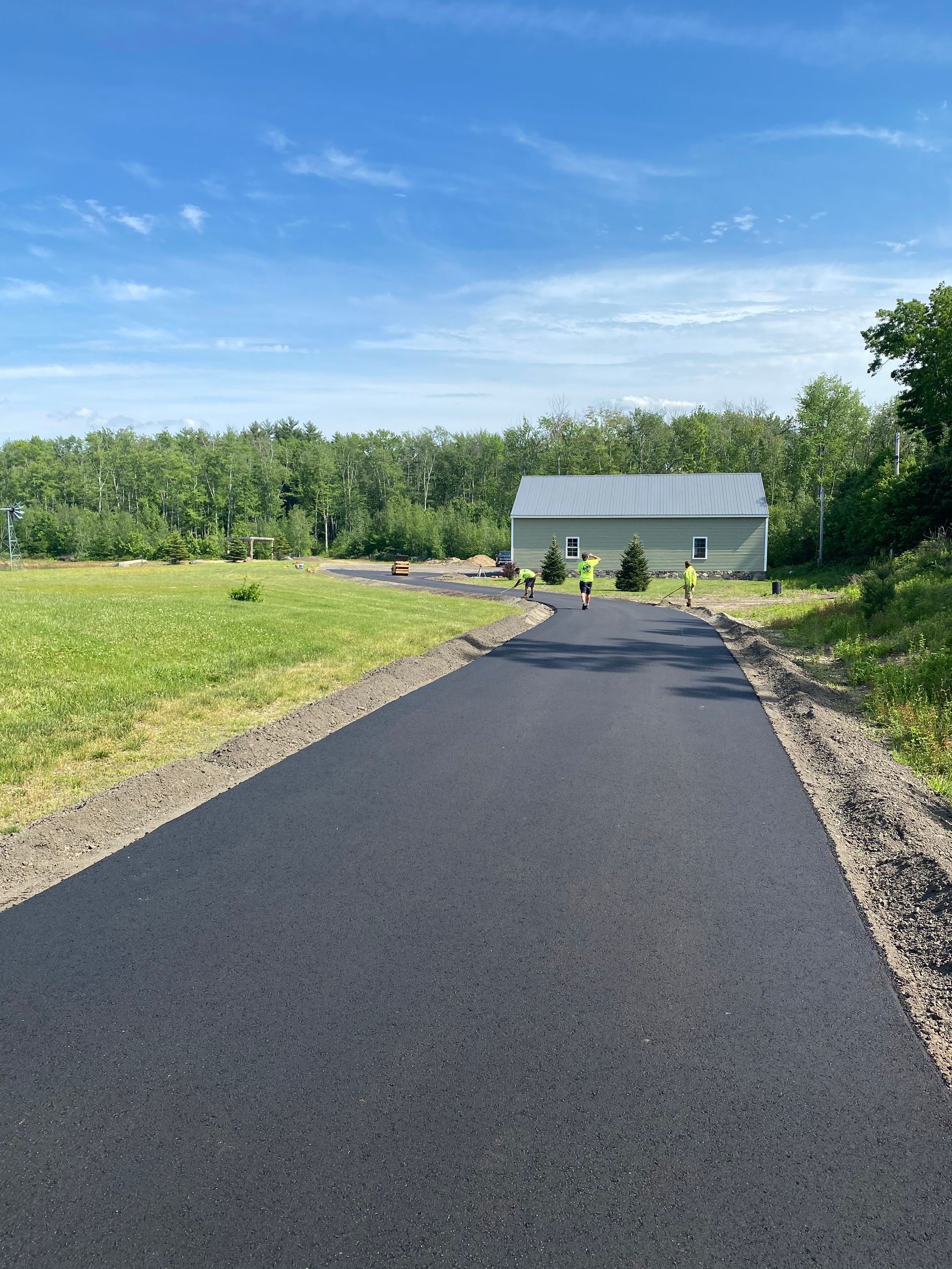 a road going through a grassy field with a house in the background