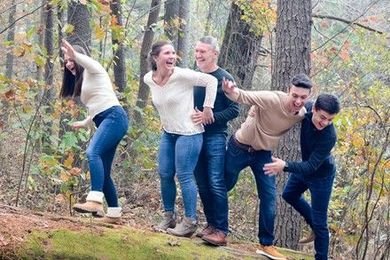 A family is standing on a log in the woods.