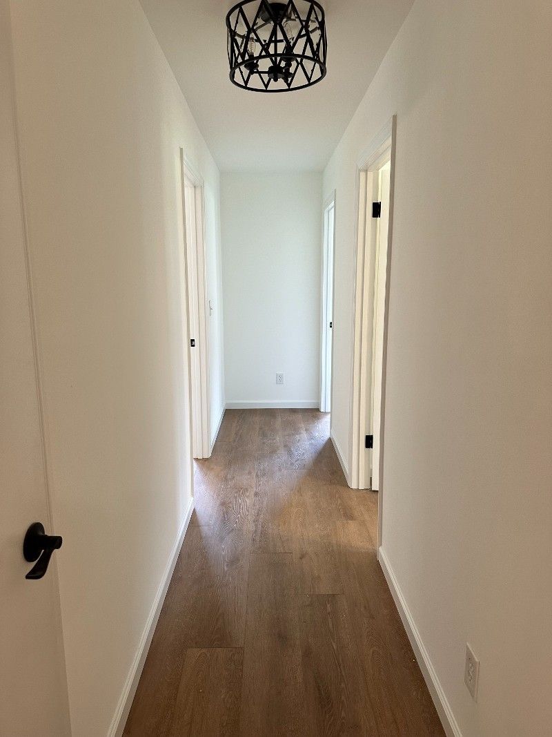 A long hallway with hardwood floors and a chandelier hanging from the ceiling.