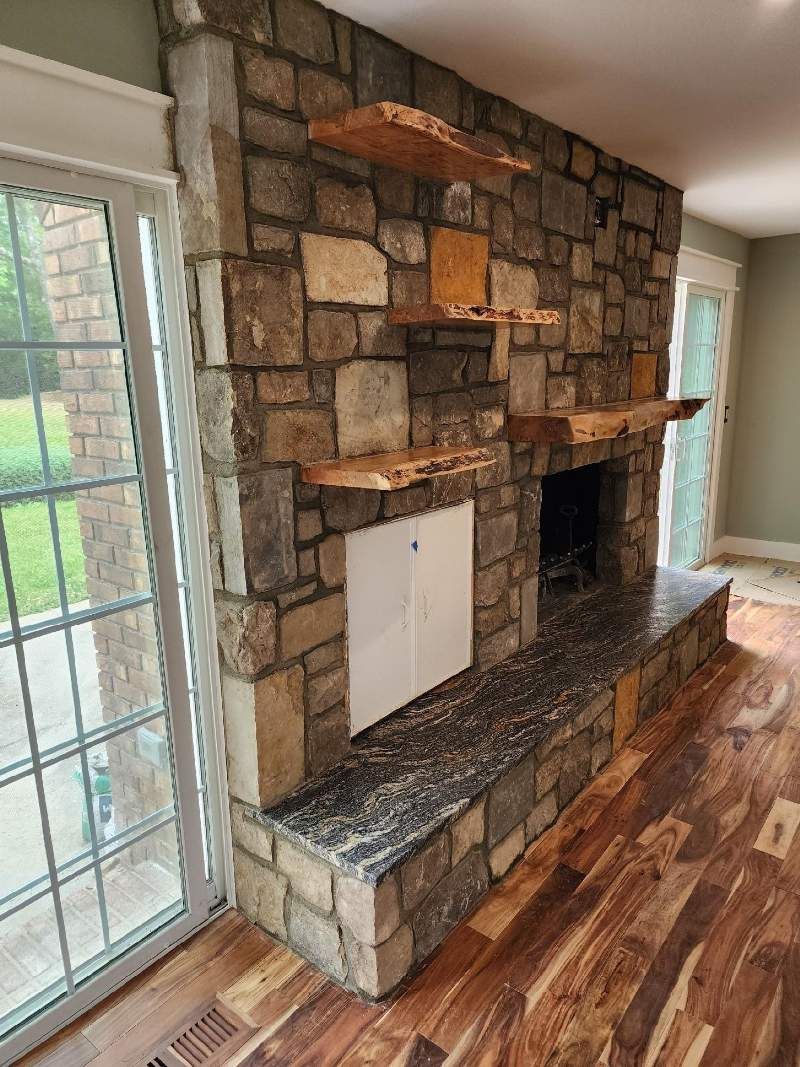 A living room with a stone fireplace and wooden floors.