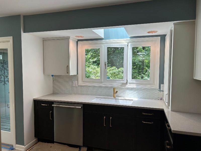 A kitchen with a sink , dishwasher , and three windows.