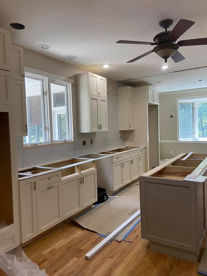 A kitchen under construction with white cabinets and a ceiling fan.