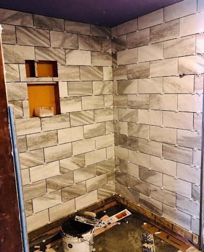 A bathroom with a tiled wall and a shelf in the corner.