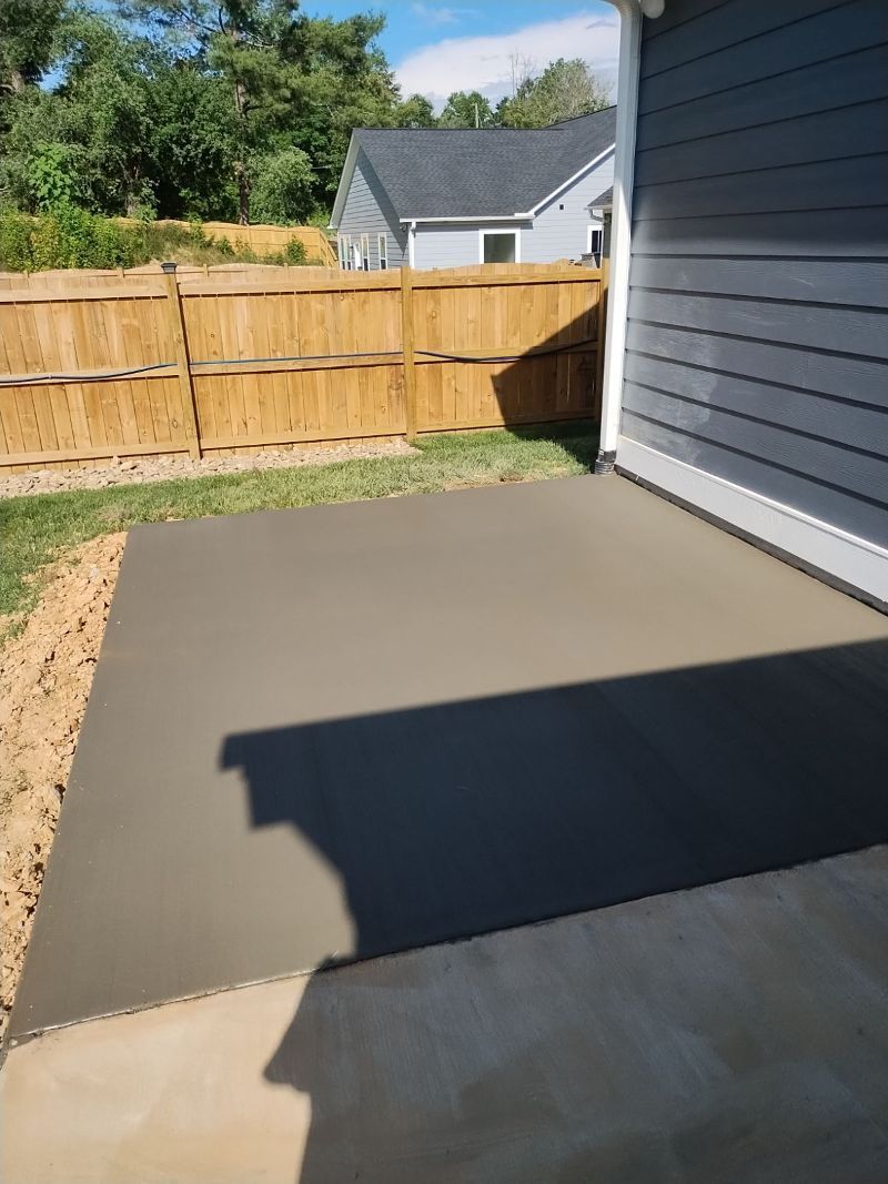 A concrete patio is being built in front of a house with a wooden fence.