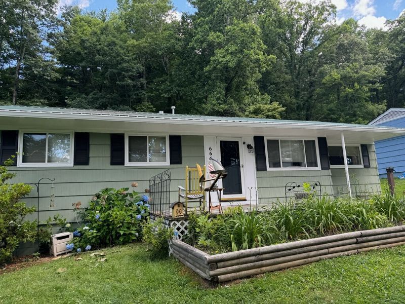 A white house with black shutters and a garden in front of it.