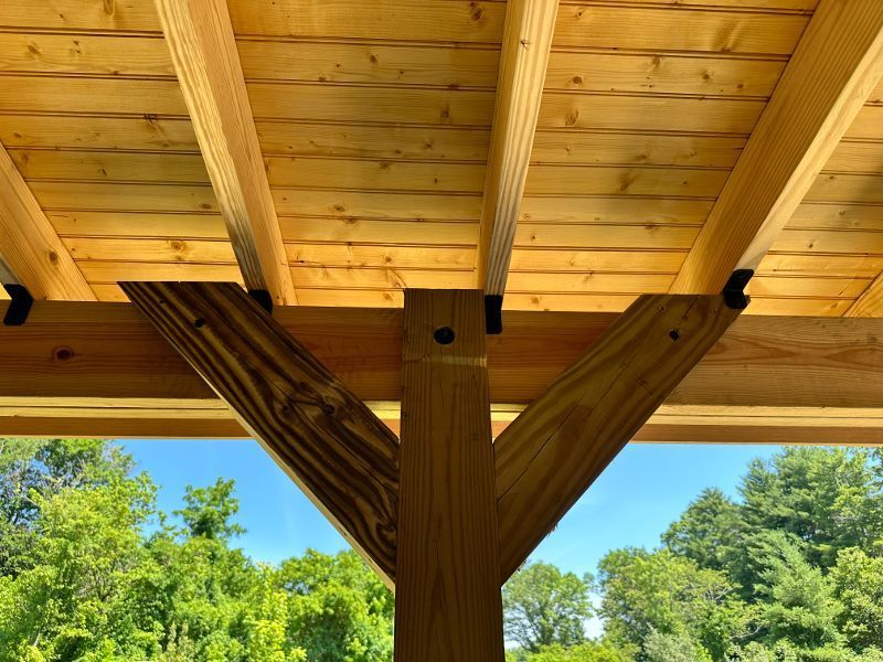 The ceiling of a wooden structure with trees in the background.