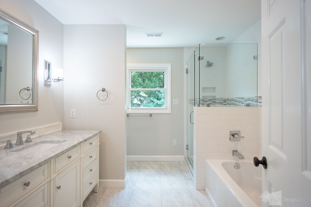 A bathroom with a tub , sink , mirror and window.